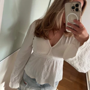 Vit blus med knytning från Gina Tricot - Supersöt vit blus/top från Gina Tricot med v-ringning och långa ärmar. Blusen har knytband i midjan men har tyvärr några små fläckar på ena armen som dock inte syns särskilt mycket i verkligheten. Perfekt till jeans eller kjol för en fräsch look. 