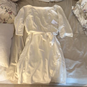 Vit kort klänning från Bubbleroom - Superfin vit kort klänning från Bubbleroom med trekvartsärm och knytband i midjan. Klänningen har en mjuk yta och en enkel, stilren design som känns både modern och klassisk. Perfekt för dig som gillar minimalistisk stil. Helt oanvänd klänning-lapp kvar!!