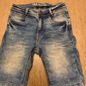 Blå jeansshorts från LAB Industries. Storlek 128 - Säljer ett par snygga och bekväma shorts från LAB Industries i färgen blå. Storlek 128, passar pojkar ca 7–8 år. Shorts med klassisk design och bra passform, perfekta för sommarens alla äventyr.  Shortsen är använda men i fint skick – inga fläckar eller hål. Mjukt och tåligt material med justerbar midja för extra komfort.  Perfekta för både lek och vardag! 