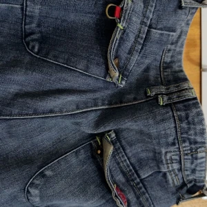 Blå jeans med fickor - Säljer ett par blå jeans som är low waisted med fickor bak. Nya köpte secondhand.