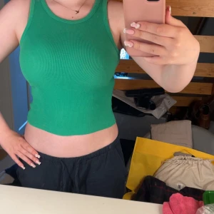 Grön ribbad linnetopp - Säljer en snygg grön ribbad linnetopp med croppad passform. Toppen har rund halsringning och är ärmlös, perfekt för varma dagar eller lager på lager. Materialet är stretchigt och sitter tight mot kroppen för en fräsch look.