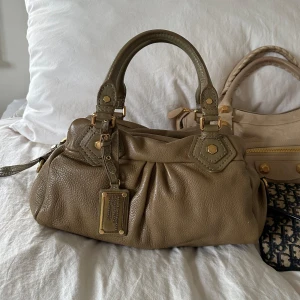 Khaki Q Classic Baby Groove väska! - Så snygg grå blåaktig klassisk handväska i nyskick från Marc by Marc Jacobs i äkta läder med gulddetaljer och dubbla handtag. Väldigt snygg färg som passar till allt, den perfekta sommarväskan som rymmer mycket men är smidig och nätt. Lilla modellen Q Classic. Inga repor eller hål på väskans läder. Otroligt välbevarad vintage modell! Perfekt för att ge en stilren touch till din outfit. Skriv privat för fler bilder. Mått 34x18x12 (undersida). Kan hämtas hemma hos mig i Nacka eller skickas🤍