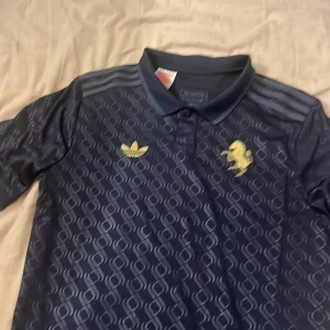 Mörkblå Adidas fotbollströja 176 - Snygg mörkblå Juventus  fotbollströja från Adidas med gul broderad logga och häst på bröstet. Tröjan har korta ärmar, krage och ett diskret geometriskt mönster i tyget. Tillverkad i lätt och ventilerande material, perfekt för träning eller match. En sjukt fet Juventus tröja med en riktigt snygg krage. Helt oanvänd. Storlek 176 (passar XS)