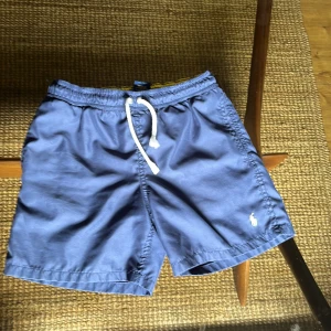 Blå badshorts Polo Ralph Lauren - Snygga marinblå badshorts från Polo Ralph Lauren, storlek M i barnstorlek (10-12). Säljer dessa på grund av att jag har vuxit ur dem. Skick 9/10 inga defekter och använd fåtal gånger. Pris kan diskuteras.
