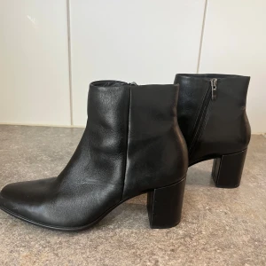 Svarta skinnstövletter från ECCO - Stilrena svarta stövletter från ECCO  med rund tå och bred klack. Skorna har dragkedja på sidan för enkel påtagning och en klassisk, minimalistisk look som passar till många outfits. Använda fåtalet gånger