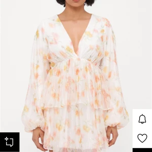 Blommig kortklänning med volang - Superfin kortklänning i vitt med blommigt mönster i pastelliga toner av rosa, gul och orange. Djup v-ringning, långa puffärmar och volangdetaljer ger en romantisk vibe. Lätt och luftig, perfekt för sommarens alla tillfällen.