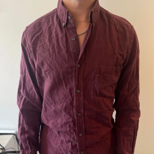 Vinröd skjorta från Massimo Dutti - Säljer en vinröd skjorta från Massimo Dutti med klassisk krage och knappstängning hela vägen. Skjortan har en bröstficka och är långärmad. Tillverkad i mjuk bomull, perfekt för dig som gillar stilrena plagg med en snygg färg.