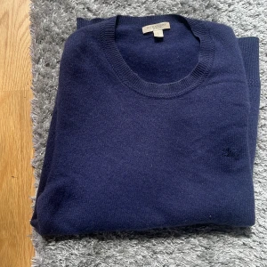 Mörkblå kashmirtröja från Burberry - Säljer en stilren mörkblå rundhalsad tröja från Burberry i mjuk kashmir. Tröjan har diskret broderad logga på bröstet och långa ärmar. Perfekt för dig som gillar klassisk och lyxig stil. Pris kan såklart diskuteras vid snabba och smidiga affärer 