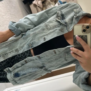 Ljusblå jeansjacka med bälte - Säljer en oversized ljusblå jeansjacka med knappar och bälte i midjan. Jackan har klassiska bröstfickor med lock och långa ärmar som kan vikas upp för en chill look. Perfekt för dig som gillar streetstyle och vill ha en avslappnad vibe.