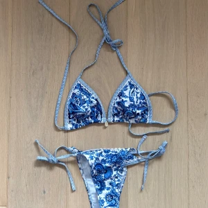 Blåvit blommig bikini - Supersöt bikini med blått och vitt blommönster. Triangeltopp med knyt i nacken och ryggen samt matchande trosa med knyt i sidorna. Perfekt för stranden och sommarens alla bad. Materialet känns mjukt och följsamt.