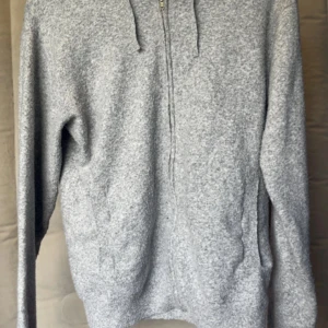 Grå hoodie från RYVLS med dragkedja - Mysig grå stickad hoodie från RYVLS med hel dragkedja framtill och huva. Tröjan har en enkel och stilren look, perfekt för chill dagar. Långärmad modell i mjukt material som känns skönt mot huden. Passar dig som gillar basic och avslappnad stil. Är runt 170 och passar mig så den är lite stor i storleken.