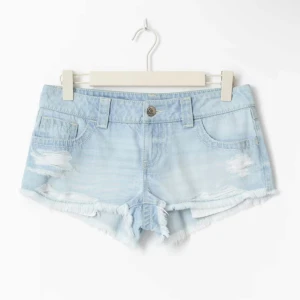 Lågmidjade ljusblå jeansshorts - snygga lågmidjade jeansshorts i ljusblå denim med slitna detaljer och fransig kant. använda 2 gånger så som nya, slutsålda överallt!!