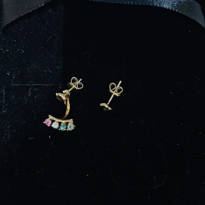 Guldpläterade örhängen med färgstenar - Snygga guldpläterade örhängen i 925 silver med en unik design. Ena örhänget har en båge med fyra små stenar i rosa, vit, grön och blå nyans. Perfekt för dig som vill ha något färgglatt och annorlunda i öronen.