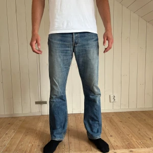 Levi's 501 blå jeans straight fit - Riktigt snygga Levi's 501 jeans i mellanblå tvätt med raka ben och rak passform.  Tillverkade i slitstarkt bomullsjeans med snygga slitningar för en avslappnad look! Denna tvätten är najs med den perfekta vintagekänslan! Tyvärr har dom slitningar i skrevet! Storlek uppskattat w29,l32