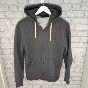 Ralph Lauren zip - Riktigt skön zip hoodie från Ralph Lauren i grå färg. Dragkedja, fickor och huva med snören – perfekt för både vardag och chill. Mjuk insida och bra passform. Använd några enstaka gånger sparsamt, hör av dig vid intresse! 🙌
