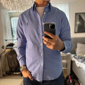 Blå skjorta Ralph Lauren Slim Fit M - Snygg blå skjorta från Ralph Lauren i slim fit-modell. Klassisk button-down krage, vita knappar och broderad logga på bröstet. Tillverkad i bomull och passar perfekt till jeans eller chinos för en clean look.