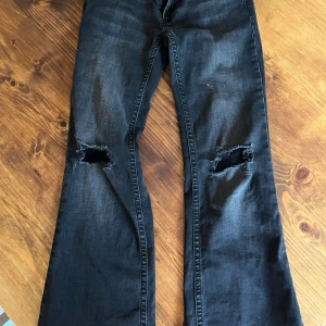 Svarta bootcut jeans med slitna knän - Snygga svarta jeans med bootcut passform och slitna hål på båda knäna. Jeansen köptes på Vinted helt nya förutom att säljaren ja köpte de av hade sytt upp de. 