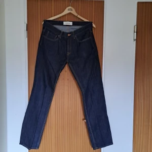 Mörkblå jeans från Dressmann - Klassiska mörkblå jeans från Dressmann med raka ben och kontrastsömmar. Jeansen har fem fickor, knappgylf och är tillverkade i robust denim. Perfekta för dig som gillar en tidlös och enkel stil.