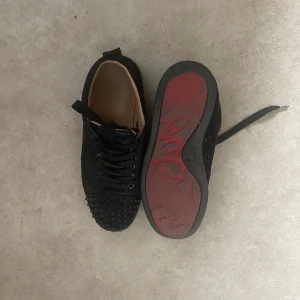 Louboutins skor - Svarta loubs med spikar på. Skorna har en röd sula undertill och är tillverkade i mocka med detaljer i skinn. Insidan är ljusbeige och designen är riktigt edgy och unik.