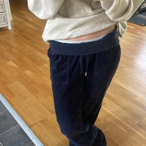 Mörkblå mjukisbyxor från Juicy Couture - Mörkblå mjukisbyxor från Juicy Couture i mjuk velour med snörning i midjan och fickor fram. Byxorna har en bakficka med knapp och broderad JC-logga. Perfekta för chill dagar och riktigt sköna att ha på sig.En metallbit som saknas, köpta här på plick. Pris kan diskuteras, skriv för fler bilder!!