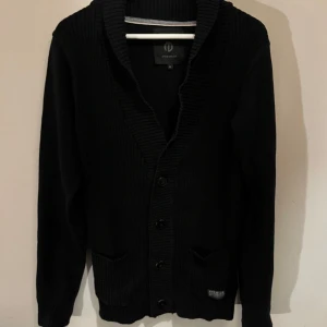 Svart kofta från Jack & Jones premium - Snygg svart kofta från Jack & Jones med ribbad krage och knappar framtill. En stilren och mångsidig tröja för alla tillfällen.