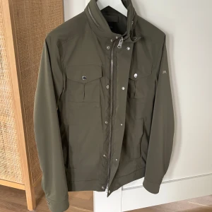 J Lindeberg Bailey Poly Stretch jacket i kanonskick - Small - Olivgrön grym jacka från J Lindeberg. Modell: Bailey Poly Stretch jacket. Nypris 3400 kr. Mkt bra skick, sparsamt använd. . Storlek Small.