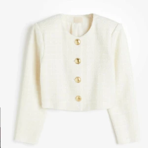 Vit kavaj från H&M - Säljer en elegant vit kavaj från H&M med stora guldknappar. Kavajen är croppad och har en stilren design med långärmade ärmar. Perfekt för en chic look.