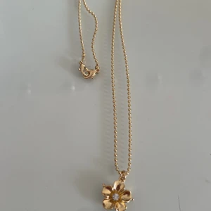 Guldhalsband med blomma - Elegant guldhalsband med en vacker blomma som hänge. Blomman har en gnistrande sten i mitten som ger en extra touch av glamour. Perfekt för att lyfta vilken outfit som helst.         Detta halsband är från ioaku ska egentligen vara två halsband men har plockat bort de ena då jag ville ha de som ett enkel halsband! Därav säljs detta för endast 200 kr. Kostar 699 nytt med båda halsband 💓💓💓
