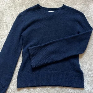 Mörkblå stickad tröja från H&M - Säljer en stilren mörkblå stickad tröja från H&M. Tröjan har långa, vida ärmar och en rund halsringning. Perfekt för kyligare dagar och lätt att matcha med olika outfits.