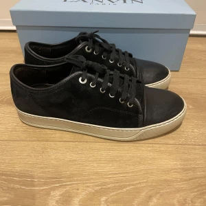 Svarta sneakers från Lanvin - Snygga svarta sneakers från Lanvin med snörning och rund tå. Skorna har en vit sula som ger en stilren kontrast. Perfekta för en avslappnad men ändå elegant look. Jag säljer dessa på grund av att de är för små för mig. De är i helt perfekt skick och original boxen är inkluderat. Är storlek 42 men passar 42-43