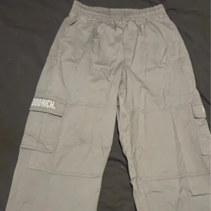 Grå parachute pants från Hoodrich - Snygga grå parachute byxor från Hoodrich med elastisk midja och flera praktiska fickor. Byxorna har en avslappnad passform och justerbara benslut för extra komfort. Perfekta för en casual look.