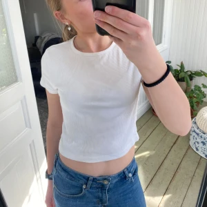 Vit ribbad croppad topp från H&M - Säljer en vit ribbad croppad topp från H&M. Toppen har korta ärmar och en rund halsringning, perfekt för en avslappnad stil. Passar bra till jeans eller kjol.