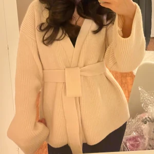 Beige ribbad cardigan jacka - Säljer en mysig beige ribbad cardigan jacka med knytbälte i midjan. Jackan har långa ärmar och en avslappnad passform, perfekt för kyliga dagar. En stilren och bekväm jacka som passar till många tillfällen.