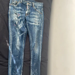 Blå jeans med färgstänk från Dsquared2 - Unika blå jeans från Dsquared2 med coola färgstänk och slitna detaljer. De har en klassisk femficksdesign och knappgylf. Perfekta för en edgy look!