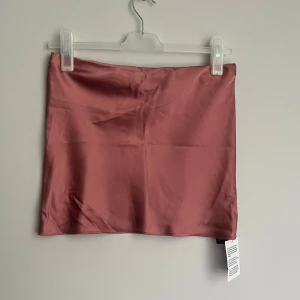 Rosa tubetopp från ASOS Design - Snygg rosa tubetopp i satin från ASOS Design. Perfekt för en stilren look med sin släta yta och mjuka glans. Kjolen har en enkel design utan detaljer för en minimalistisk stil.