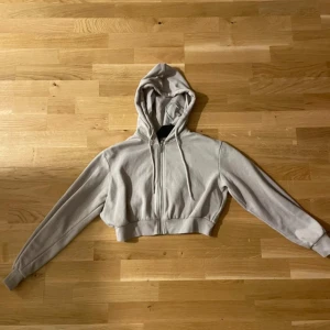 Beige croppad hoodie - Säljer en beige croppad hoodie med dragkedja och huva. Perfekt för en avslappnad stil. Den har långa ärmar och en mjuk känsla.