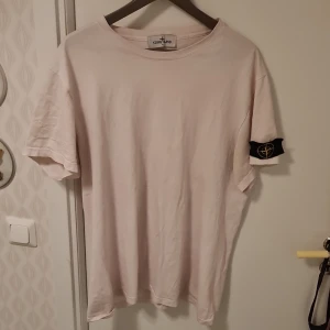 Beige t-shirt från Stone Island - Säljer en stilren beige t-shirt från Stone Island. Den har korta ärmar och en klassisk rund halsringning. Perfekt för en avslappnad look med den ikoniska loggan på ärmen.