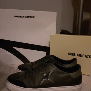Svarta sneakers från Axel Arigato - Snygga svarta sneakers från Axel Arigato med en stilren design. Skorna har snörning och en vit sula som kontrasterar mot det svarta. Perfekta för en trendig look.