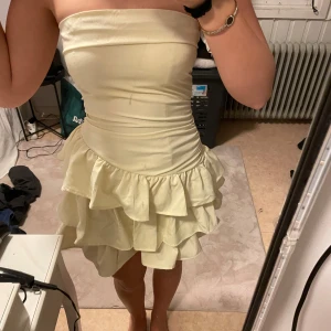Ljusgul axelbandslös klänning - Säljer en söt ljusgul axelbandslös klänning med volanger. Perfekt för sommarens fester. Klänningen har en tight passform upptill och en volangkjol som ger en lekfull look.