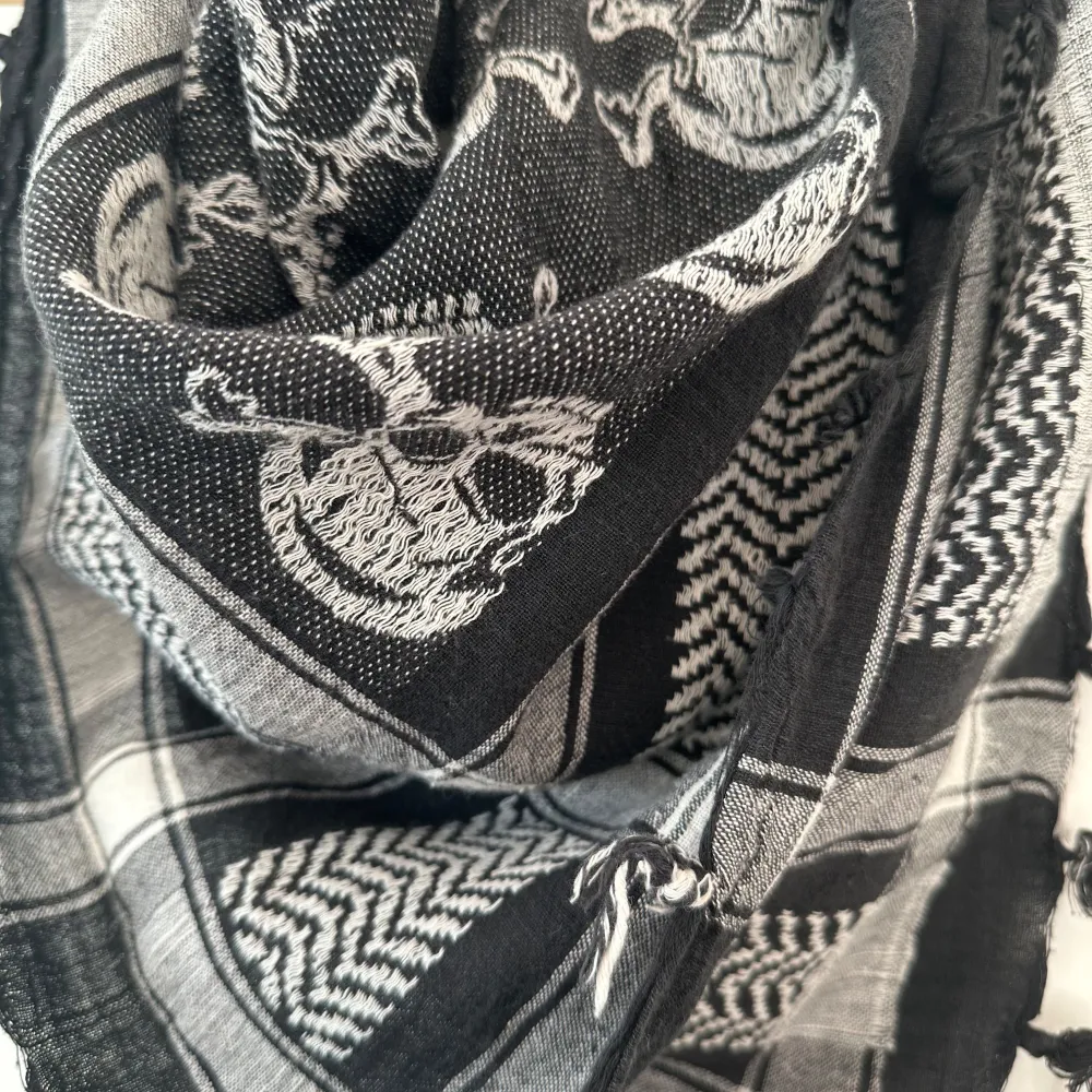 Snygg svart och vit sjal / scarf / halsduk med ett coolt dödskallemönster. Den har fransar längs kanterna och ett rutigt mönster som ger en extra touch. Perfekt för att ge din outfit en edgy stil.. Muu.