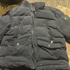 Svart pufferjacka från Outernational - Säljer en svart pufferjacka från Outernational. Jackan har en dragkedja framtill och praktiska fickor med knappar. Perfekt för kyligare dagar med sin vadderade design.