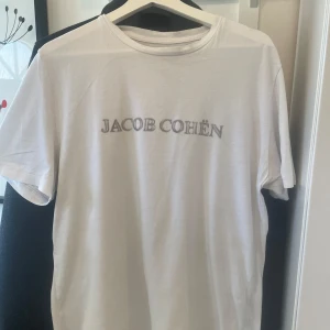 Vit t-shirt från Jacob Cohën - Säljer en stilren vit t-shirt från Jacob Cohën med märkets logga tryckt på framsidan. Sitter väldigt bra, inte för tajt och inte för loose. Perfekt nu till sommaren! Storleken på t-shirten är M och passar er som är runt 180-187. T-shirten är väl använd men har tagits väl hand om. Köpt för 3000 kr på designer-butiken Thomas i Halmstad, säljer för endast 800kr! Endast t-shirten medföljer. Har ni frågor eller funderingar är det bara att ställa dem!