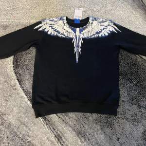 Snygg svart tröja från Marcelo Burlon med ett iögonfallande vitt och blått vingmönster över axlarna. Perfekt för dig som vill sticka ut med en unik design. Tröjan har långa ärmar och en bekväm passform.