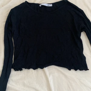 Svart ribbad tröja - Säljer en svart ribbad tröja med långa ärmar och en croppad design. Perfekt för en stilren look. Tröjan har en enkel och bekväm passform. Fin på sommaren