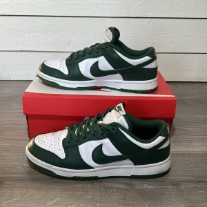 Nike Dunk i grönt och vitt - Snygga Nike Dunk sneakers i en fräsch grön och vit färgkombination. Skorna har en klassisk design med snörning och rund tå. Perfekta för en stilren look.