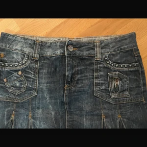 Jeanskjol med nitar och fickor - Snygg jeanskjol i mörkblå denim med dekorativa nitar och fickor fram och bak. Perfekt för en avslappnad stil.