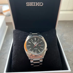 Seiko SNKL45 Klocka - Stilren klocka från Seiko, modellen SNKL45, som passar till det mesta, väldigt lätt och skön som vardagsklocka. Automatisk klocka med dag och datum. 3 språk. Knappt använd, väldigt fint skick. Lite hairlines/mindre repor på armbandet, men felfritt glas.  Bara att skicka om fler bilder önskas. Kommer med box och extra links. Uppskattas till 37mm