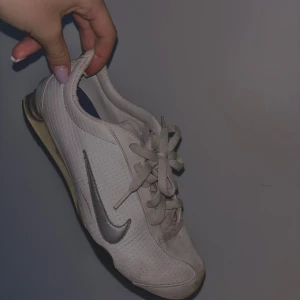 Vita Nike sneakers med silverdetaljer - Säljer ett par vita Nike sneakers med silverfärgad swoosh. Skorna har snörning och en rund tå. Perfekta för en sportig look. Lite smutsig men inte något våtservetter inte kan fixa!! 
