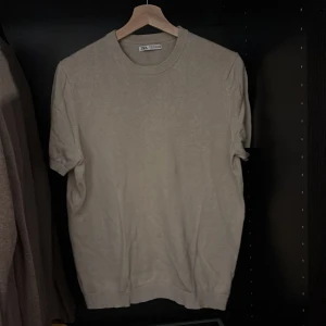 Beige kortärmad tröja från Zara - Säljer en stilren beige kortärmad tröja från Zara. Tröjan är tillverkad i en blandning av linne och bomull, vilket ger en skön och luftig känsla. Perfekt för varmare dagar. Rund halsringning och ribbade kanter för en klassisk look. Bra skick, inga defekter. Skriv vid frågor