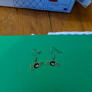 Örhängen med krabbor - Unika örhängen i form av krabbor med svart och guld detaljer. Perfekta för att ge en lekfull touch till din stil. De har en krok för enkel användning.